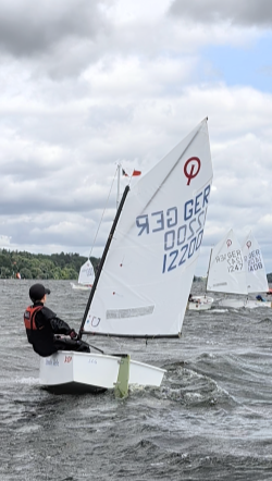 Optimist GER 12200 mit jungem Segler in Ausreitlage bei kräftigem Wind und Welle, weitere Optis im Hintergrund